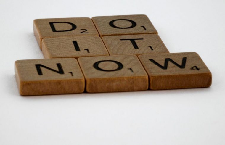 Wooden Scrabble tiles spelling 'Do It Now' on a white background. Motivational concept.