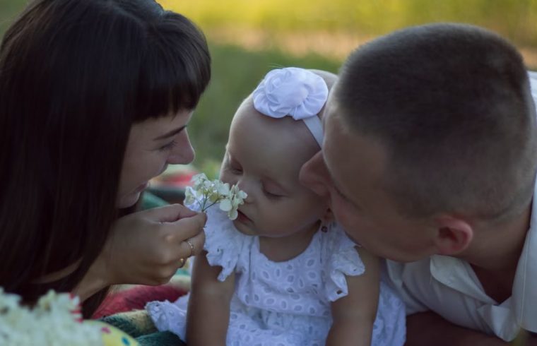 A loving family moment with parents and baby at a sunny outdoor picnic.